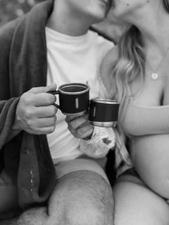 Pareja besándose mientras sostienen tazas de café