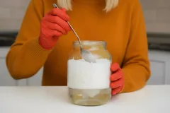 Persona con guantes rojos saca azúcar de un frasco grande en una cocina moderna