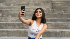 Mujer joven sonriente tomando selfie con celular sentada en la escalera